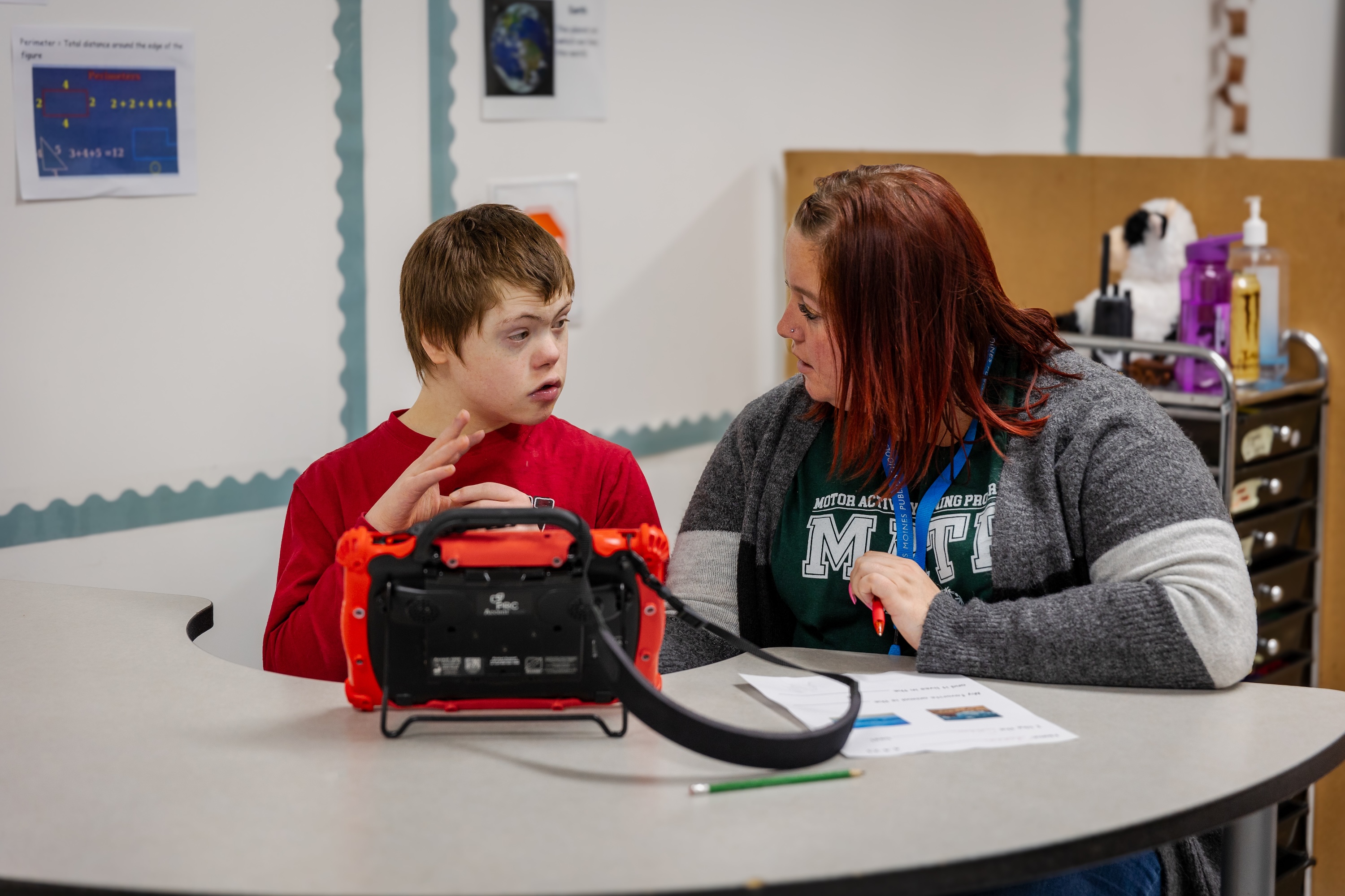 A teacher and a student with intellectual disabilities talk while sitting at a desk